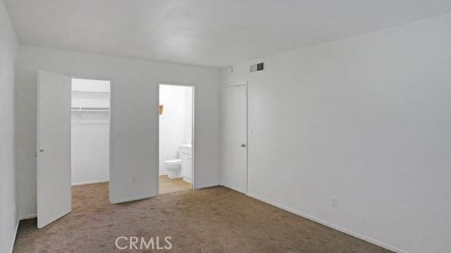 unfurnished bedroom with carpet, visible vents, connected bathroom, a walk in closet, and a closet