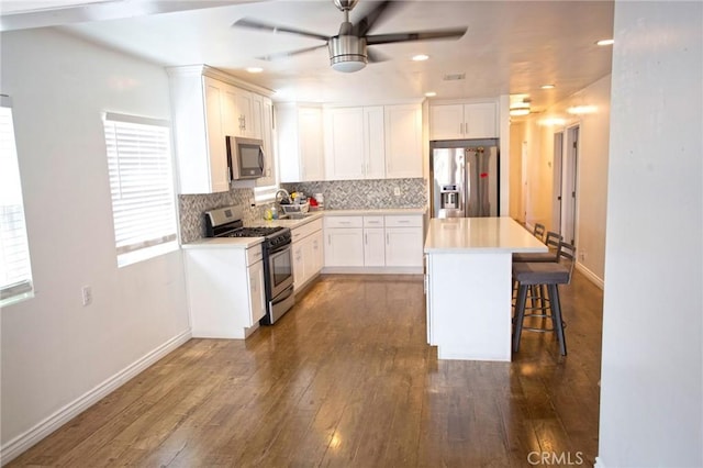kitchen with dark wood-style flooring, a ceiling fan, a kitchen bar, stainless steel appliances, and decorative backsplash