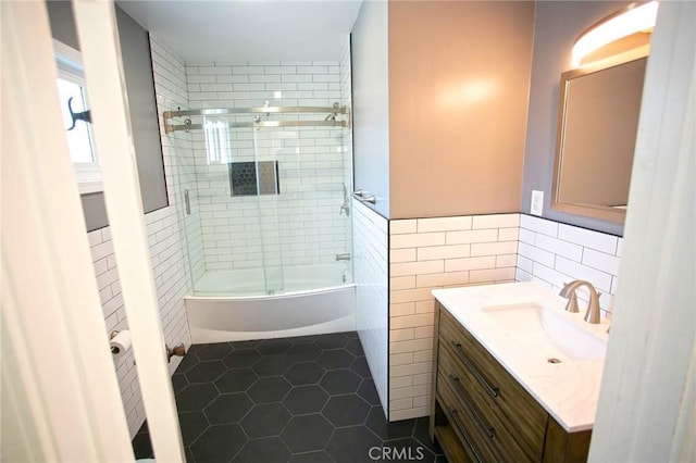 bathroom featuring shower / bath combination with glass door, vanity, tile patterned flooring, wainscoting, and tile walls