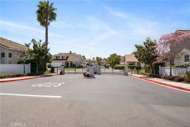 view of street with a residential view, street lights, a gated entry, a gate, and sidewalks