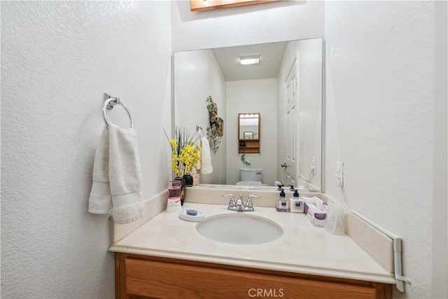 bathroom featuring a textured wall, vanity, and toilet