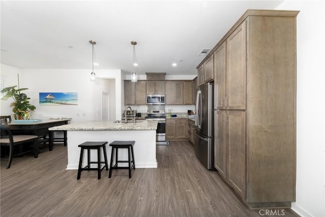 kitchen with a breakfast bar, light stone counters, a sink, stainless steel appliances, and dark wood-style floors