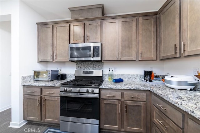 kitchen featuring baseboards, stainless steel appliances, dark wood-type flooring, a toaster, and light stone counters
