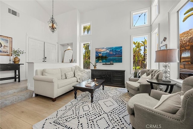 living area with visible vents, baseboards, an inviting chandelier, light wood finished floors, and high vaulted ceiling