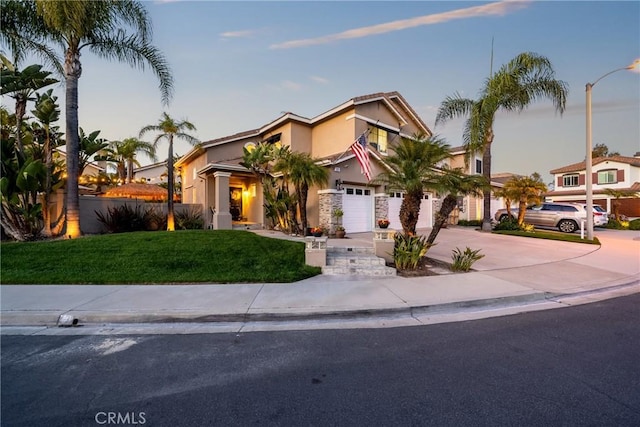 view of front of house with stucco siding, driveway, an attached garage, a front lawn, and fence