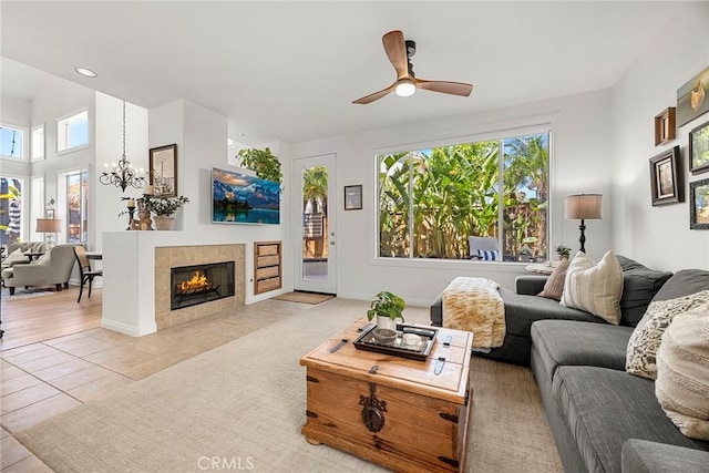 living area with a fireplace, ceiling fan with notable chandelier, light tile patterned flooring, and a healthy amount of sunlight