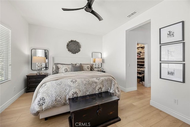 bedroom with baseboards, a spacious closet, visible vents, ceiling fan, and light wood finished floors