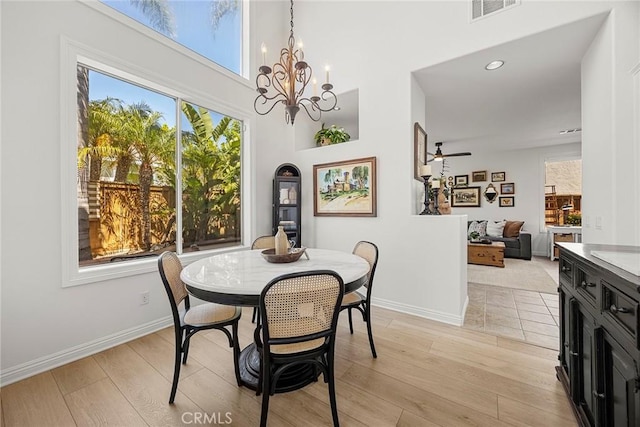 dining room with light wood-style floors, visible vents, a high ceiling, and baseboards