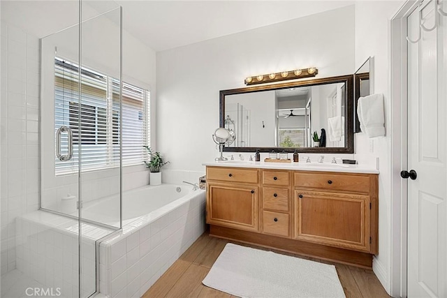 full bath featuring a bath, wood finished floors, double vanity, and a sink