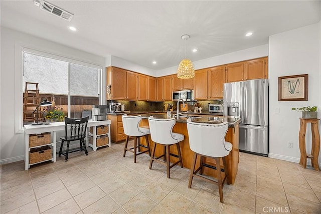 kitchen with tasteful backsplash, a kitchen breakfast bar, a kitchen island with sink, visible vents, and appliances with stainless steel finishes