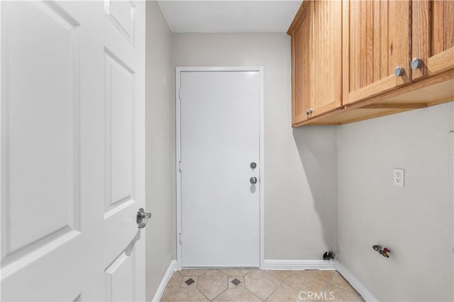 clothes washing area featuring cabinet space, light tile patterned floors, and baseboards