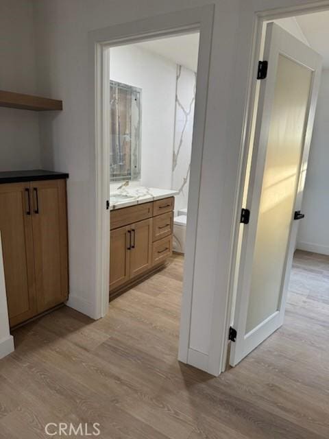 corridor featuring light wood-type flooring, baseboards, and a sink