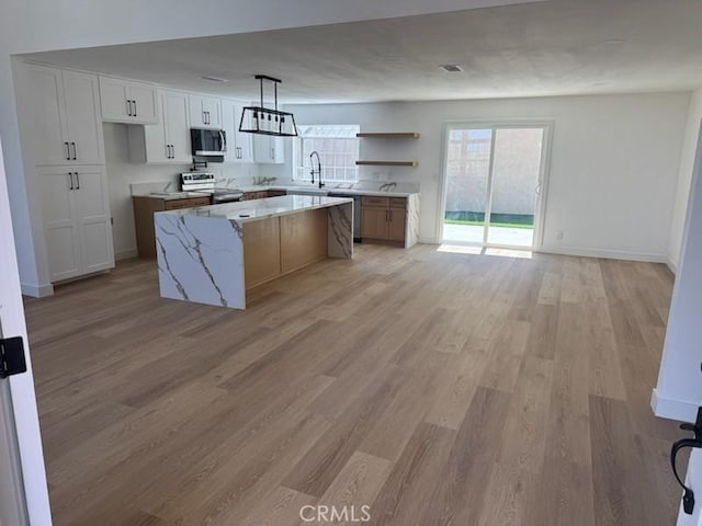 kitchen featuring a center island, open shelves, open floor plan, stainless steel appliances, and light wood-style flooring