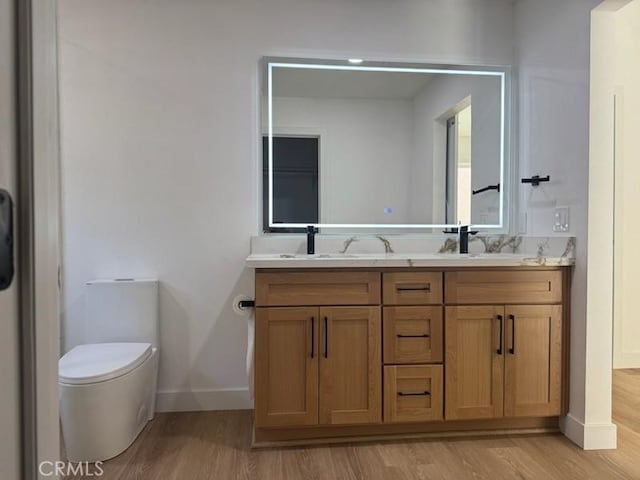 full bathroom with a sink, double vanity, toilet, baseboards, and wood finished floors