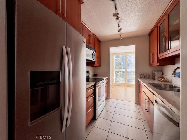 kitchen featuring a textured ceiling, a sink, brown cabinets, stainless steel appliances, and rail lighting