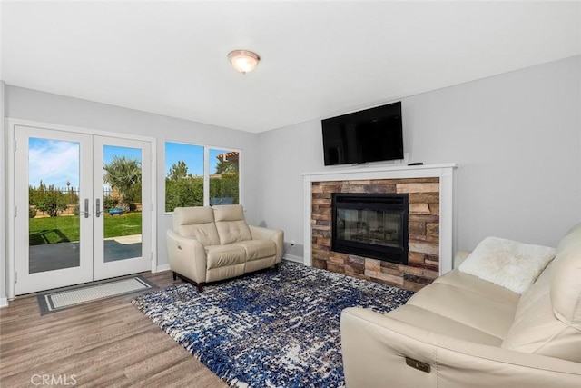 living area featuring a glass covered fireplace, french doors, baseboards, and wood finished floors