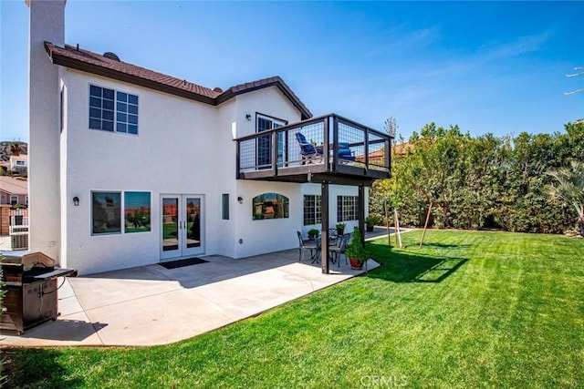 rear view of property featuring stucco siding, a lawn, a patio, a balcony, and french doors