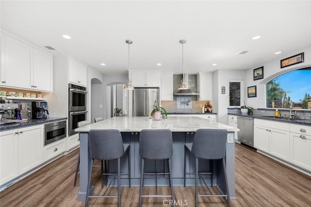 kitchen featuring tasteful backsplash, wall chimney exhaust hood, stainless steel appliances, arched walkways, and a sink