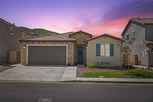 ranch-style home with an attached garage, stone siding, a tile roof, concrete driveway, and stucco siding