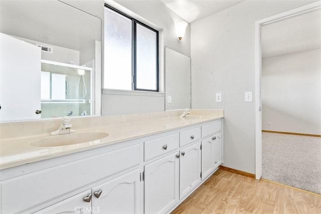 bathroom featuring a sink, double vanity, a shower stall, wood finished floors, and visible vents