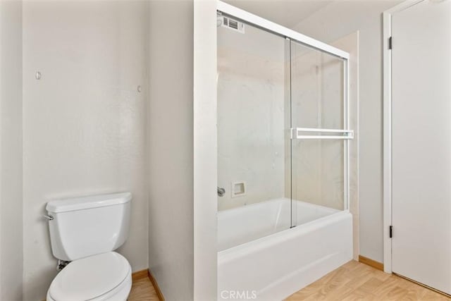 bathroom featuring baseboards, shower / bath combination with glass door, visible vents, and toilet