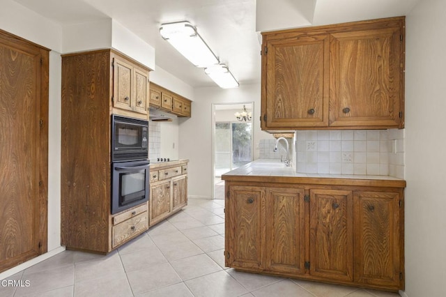 kitchen featuring tasteful backsplash, brown cabinetry, light countertops, black appliances, and a sink