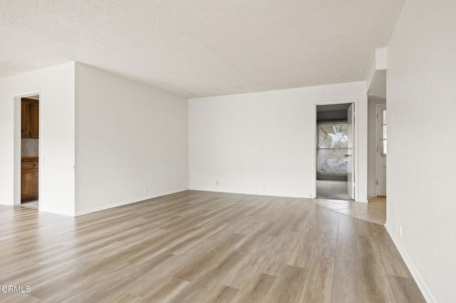 empty room featuring a textured ceiling, light wood finished floors, and baseboards