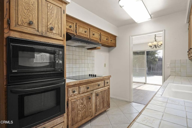 kitchen with tasteful backsplash, under cabinet range hood, brown cabinets, black appliances, and tile countertops