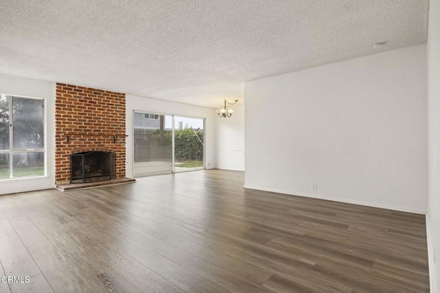 unfurnished living room with wood finished floors, a notable chandelier, a textured ceiling, and a fireplace