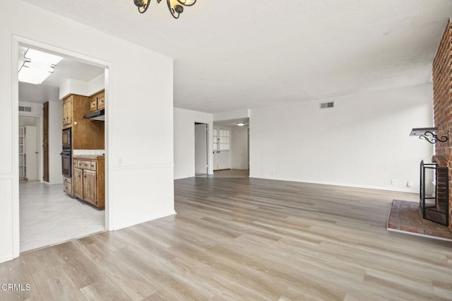 unfurnished living room featuring visible vents, a notable chandelier, and light wood-type flooring