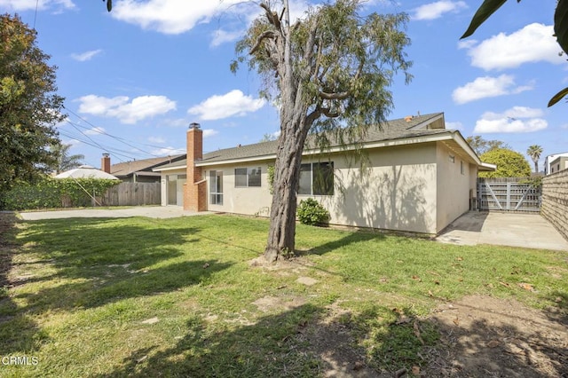 rear view of house featuring a garage, fence, a lawn, and a patio area