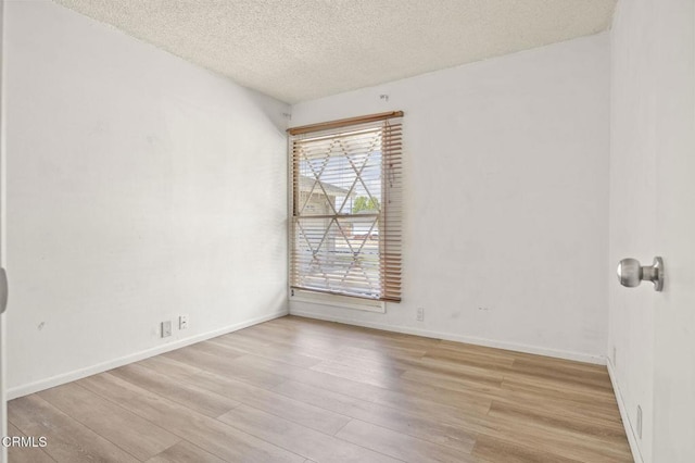empty room with light wood finished floors, a textured ceiling, and baseboards
