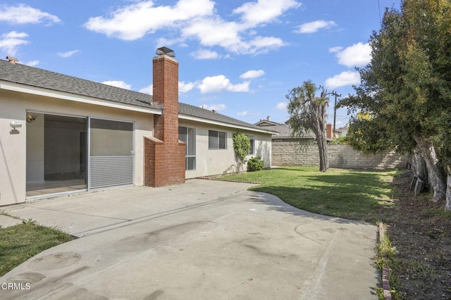 rear view of property featuring a patio, a chimney, stucco siding, fence, and a yard