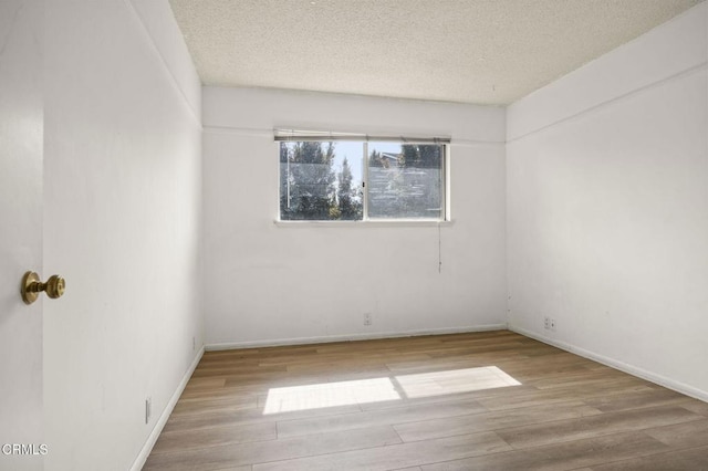 empty room with a textured ceiling, wood finished floors, and baseboards