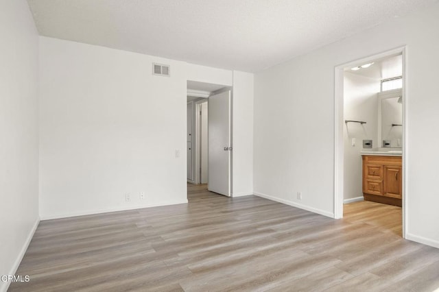 unfurnished bedroom featuring visible vents, light wood-type flooring, ensuite bathroom, and baseboards