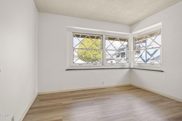 spare room with a textured ceiling, wood finished floors, and baseboards
