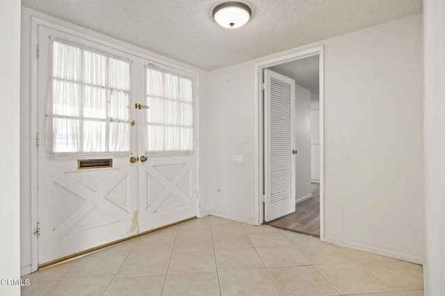 doorway to outside featuring baseboards, light tile patterned floors, and a textured ceiling
