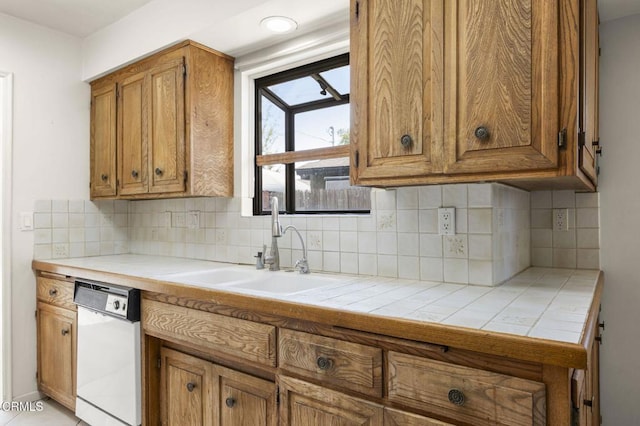 kitchen featuring tile counters, a sink, white dishwasher, and brown cabinetry