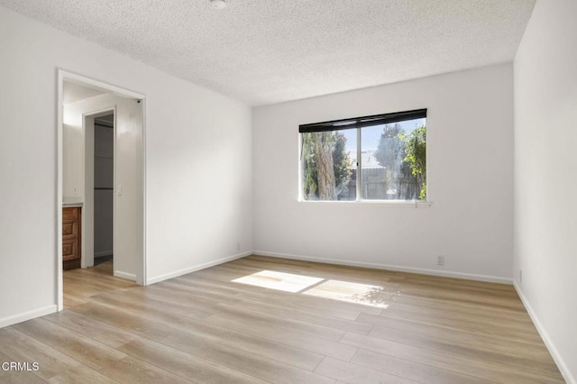 spare room featuring a textured ceiling, baseboards, and light wood-style floors