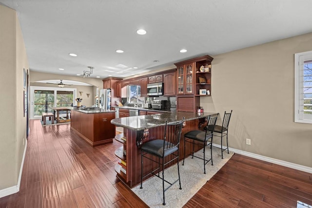 kitchen with baseboards, a center island, a breakfast bar area, stainless steel appliances, and arched walkways