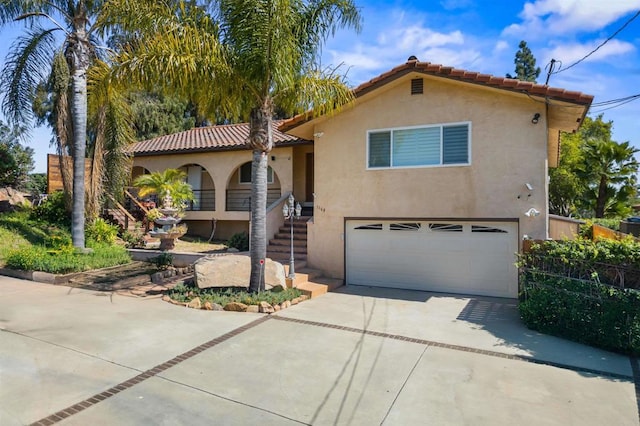 mediterranean / spanish home with a tiled roof, stucco siding, stairs, an attached garage, and concrete driveway