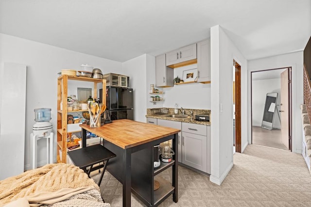 kitchen featuring a sink, freestanding refrigerator, light carpet, and butcher block counters