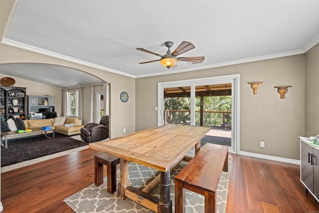 dining space with dark wood-type flooring, arched walkways, a ceiling fan, and ornamental molding