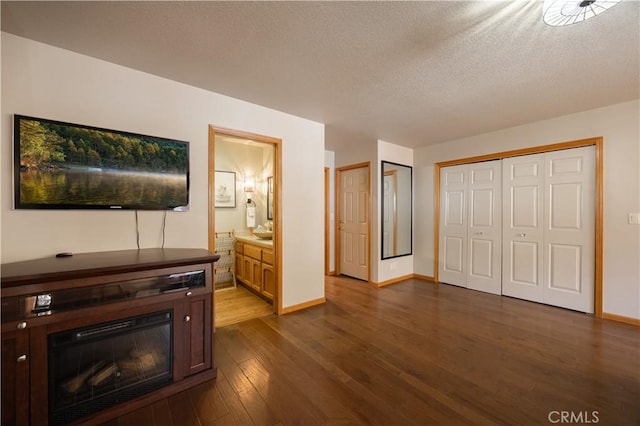 living area featuring a glass covered fireplace, baseboards, a textured ceiling, and dark wood finished floors