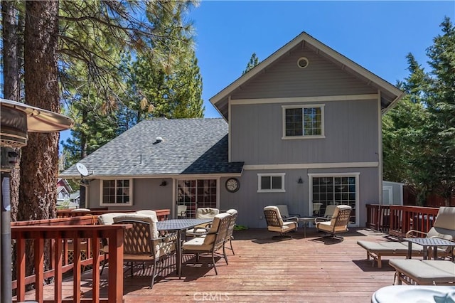 rear view of house with outdoor dining area, a wooden deck, and roof with shingles