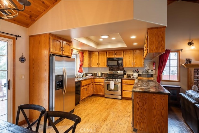 kitchen featuring light wood finished floors, a peninsula, dark stone countertops, brown cabinets, and black appliances