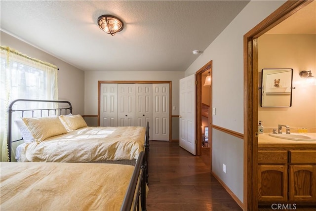 bedroom with ensuite bathroom, a sink, a textured ceiling, a closet, and dark wood finished floors