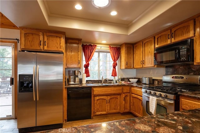 kitchen with a tray ceiling, a sink, brown cabinets, and black appliances