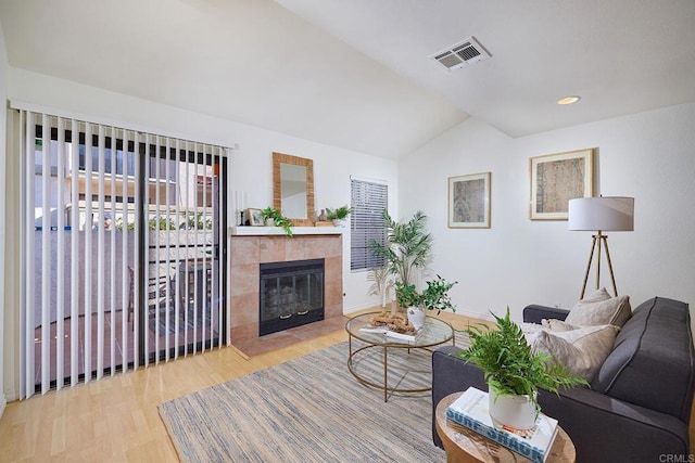 living area with visible vents, a tile fireplace, wood finished floors, baseboards, and lofted ceiling