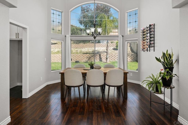 dining room featuring a wealth of natural light, dark wood finished floors, a chandelier, and a towering ceiling